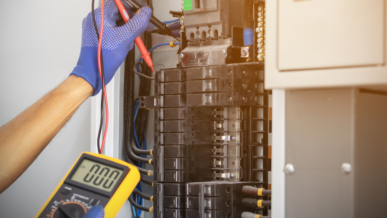 Electrician testing electrical panel with multimeter, wearing blue gloves.