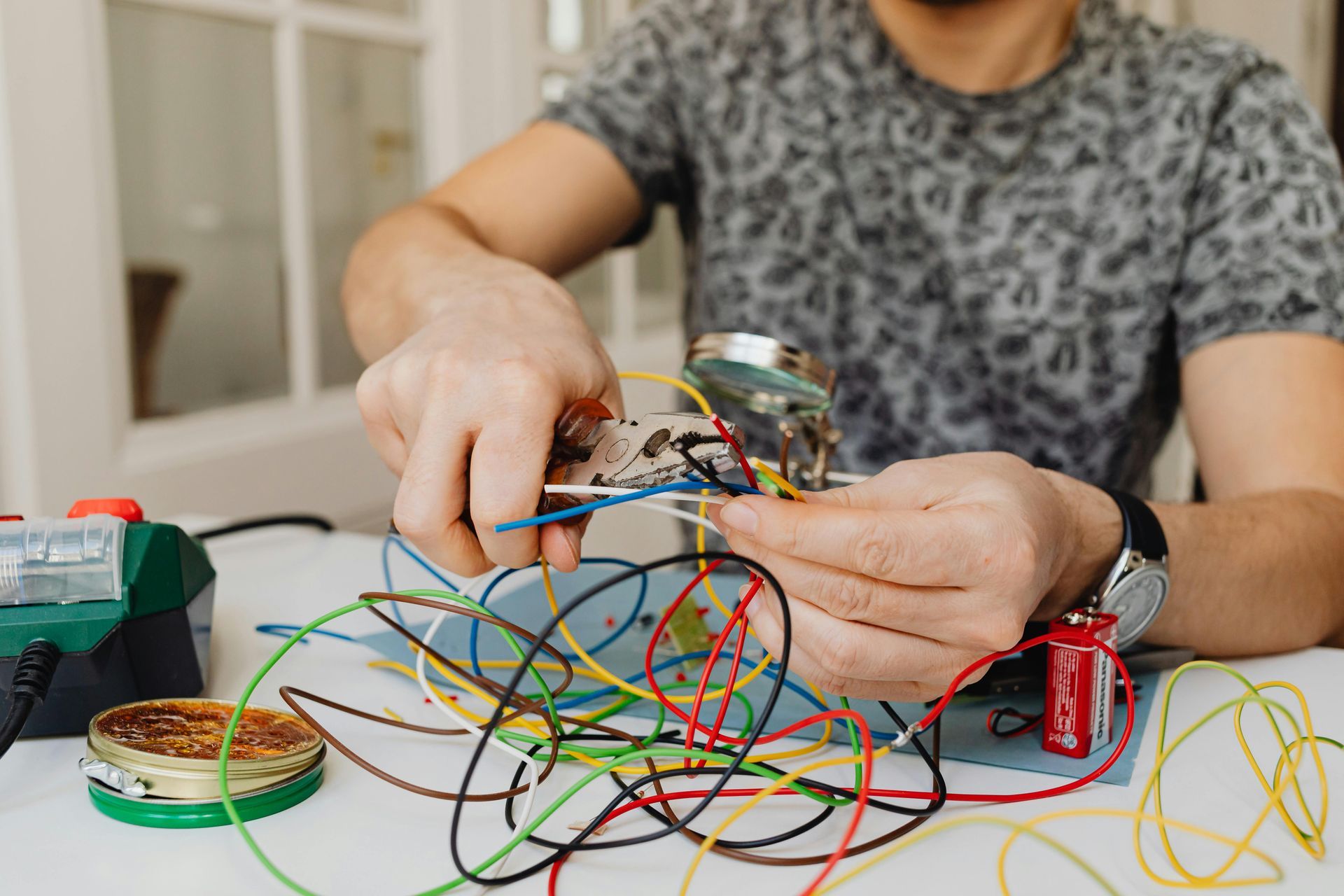 Person soldering wires on circuit board at a table, with many colored wires.