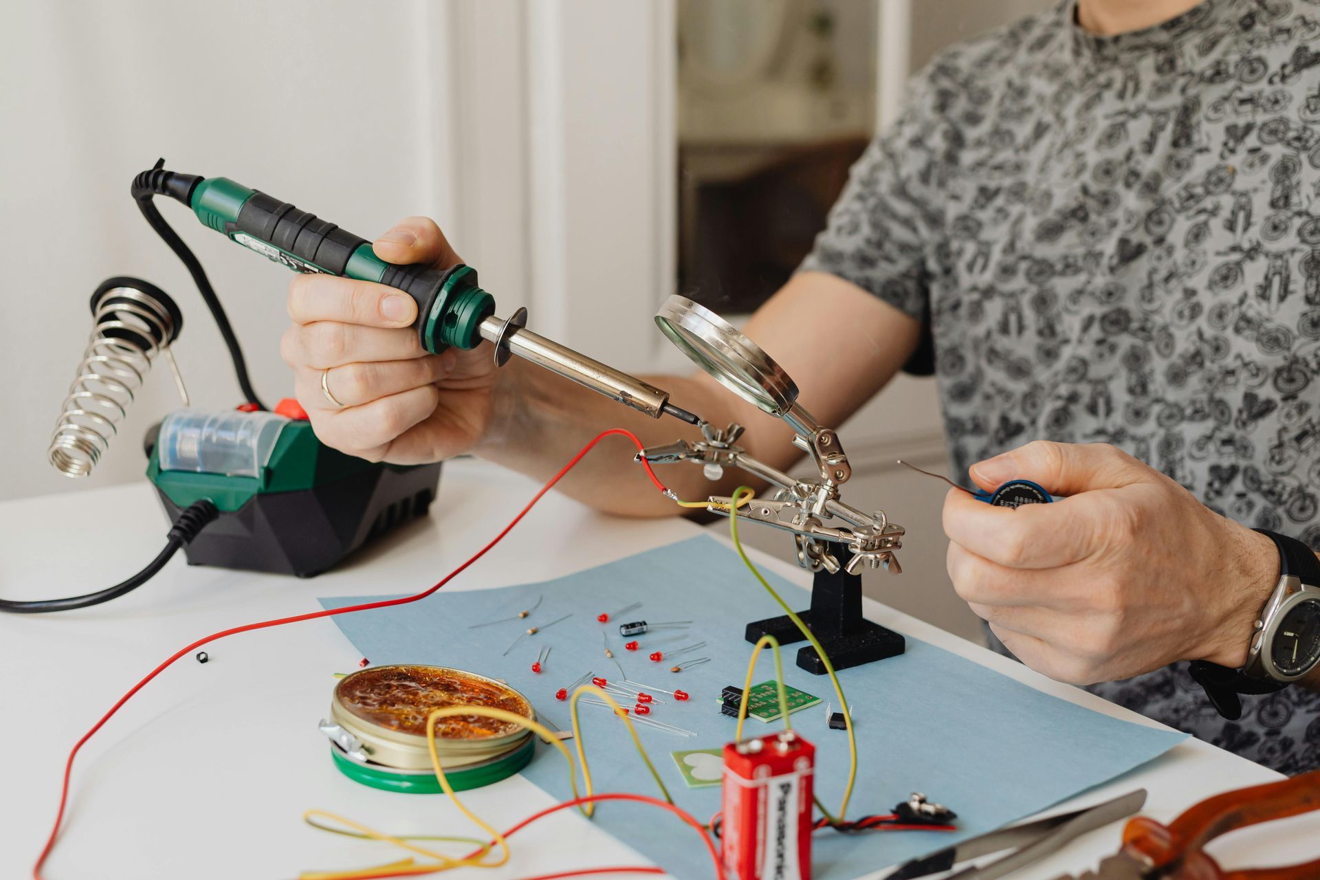 Person soldering electronic components on a circuit board; table, tools.