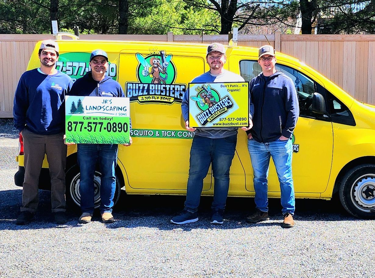 Four men stand in front of a yellow van, each holding a sign. The van is branded with