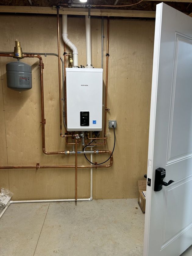 A white water heater is installed in a basement next to a door.