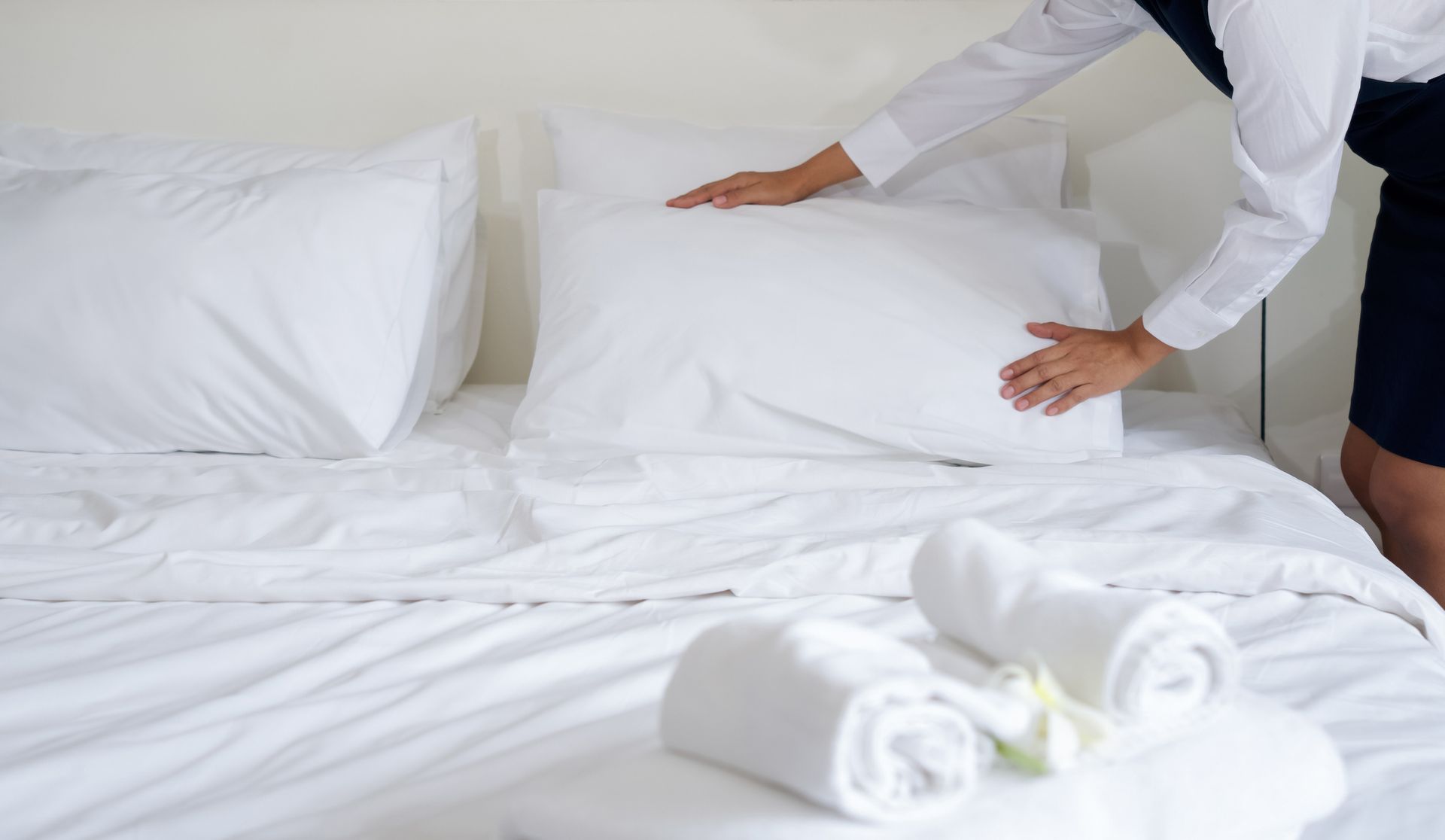 A woman is making a bed with white sheets and pillows.