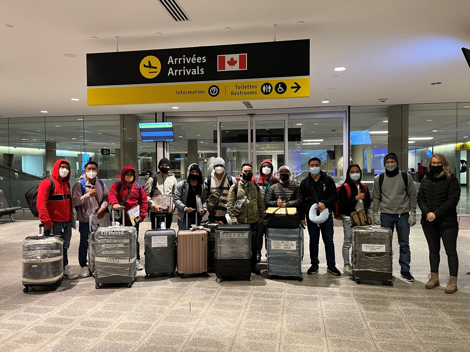 Un groupe de personnes portant des masques se tient devant des bagages dans un aéroport.