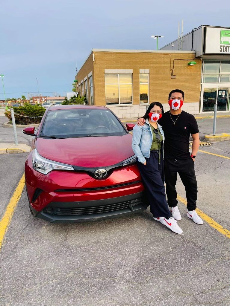 Un homme et une femme portant des masques se tiennent devant une voiture rouge.