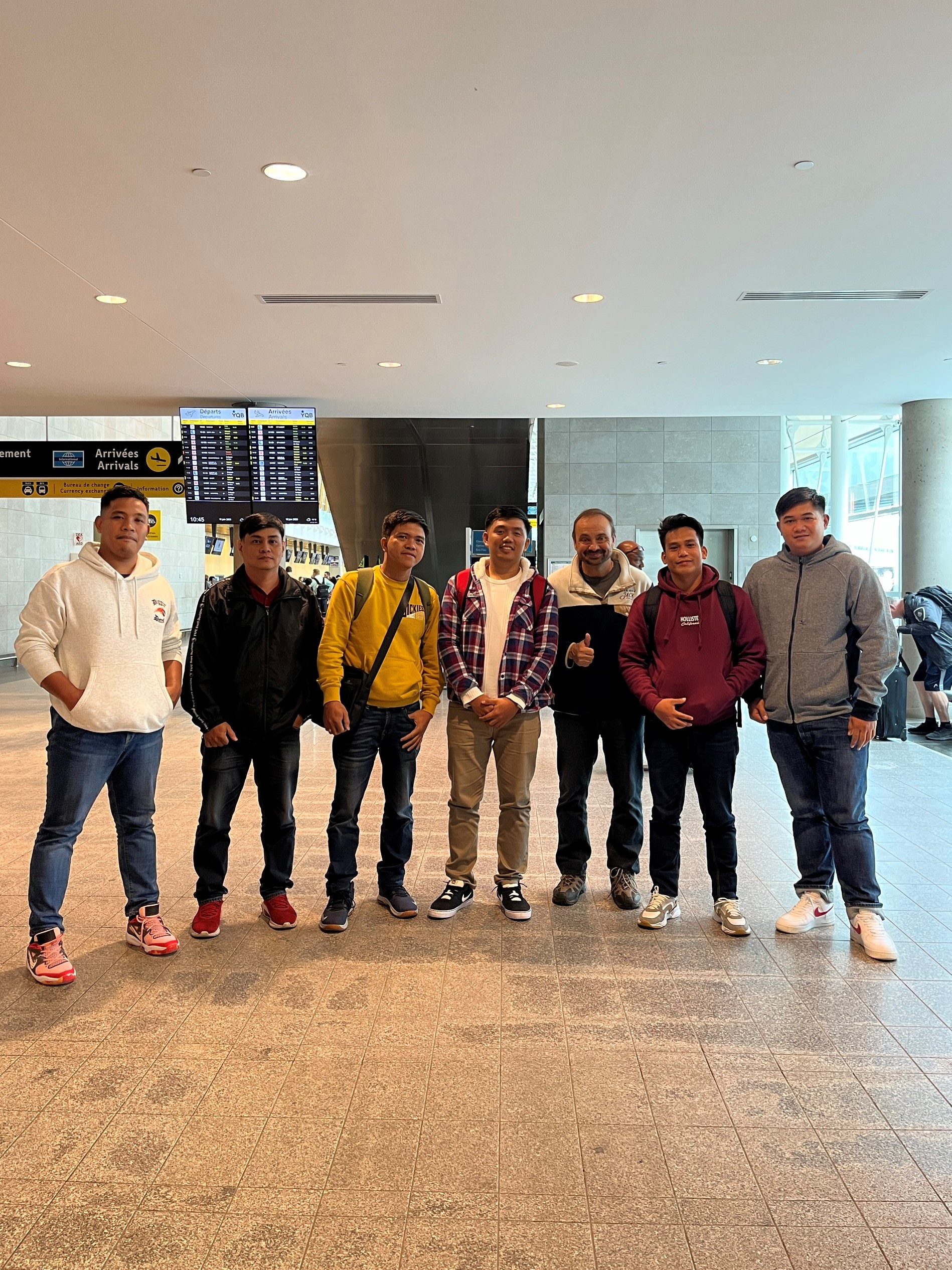 Un groupe de jeunes hommes se tiennent côte à côte dans un aéroport.