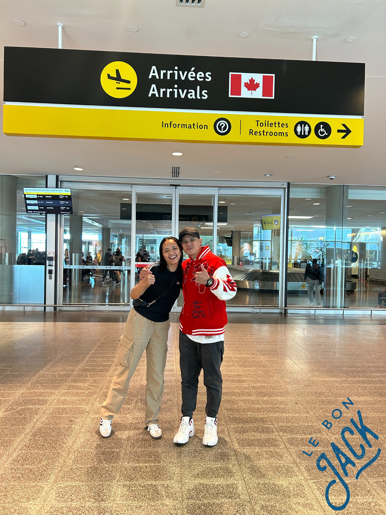 Un homme et une femme posent pour une photo devant un panneau indiquant arrivées