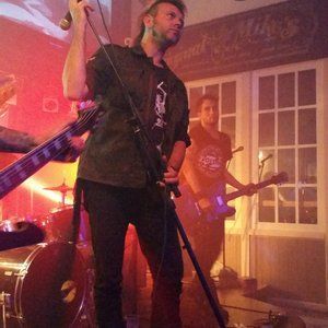 A man is singing into a microphone while playing a guitar in a band.