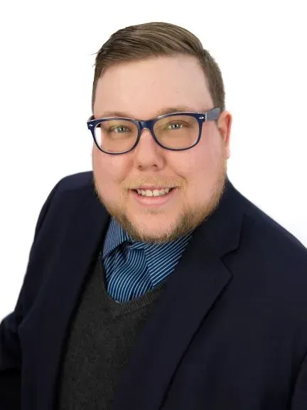 A man wearing glasses and a suit is smiling for the camera.