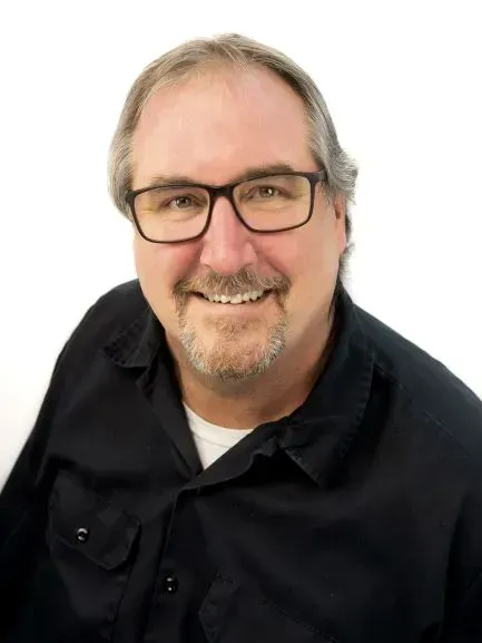 A man wearing glasses and a black shirt is smiling for the camera.