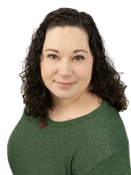 A woman with curly hair is wearing a green sweater and smiling.