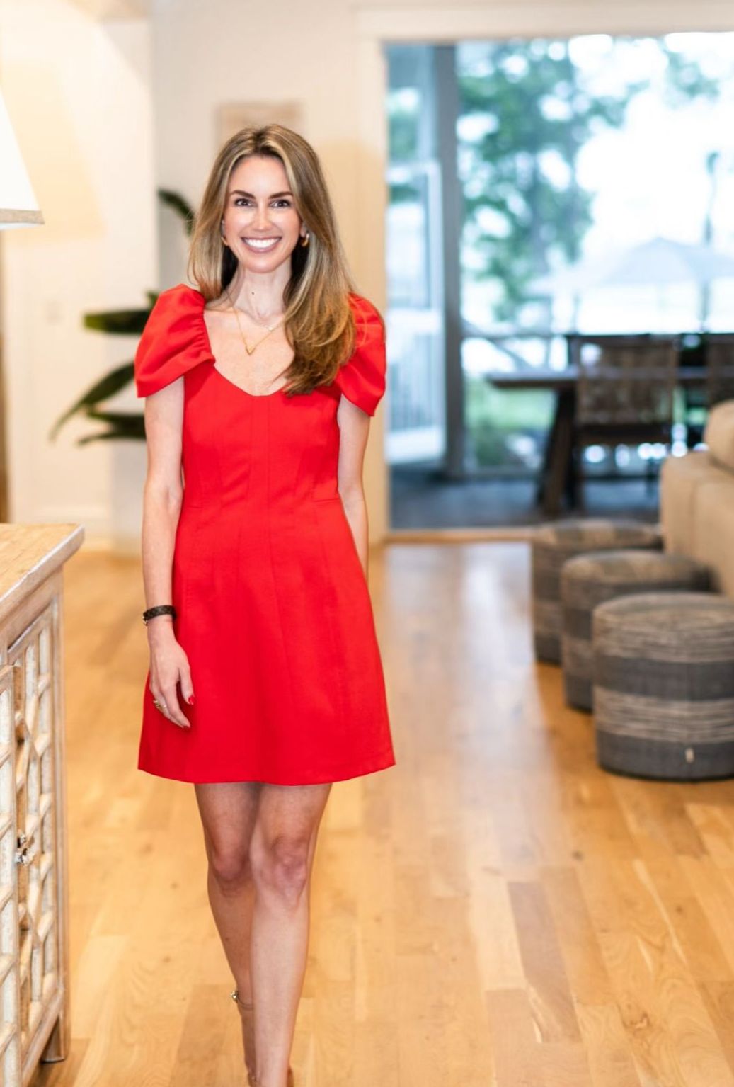 Ashley Cashon in a red dress smiling and walking toward the camera inside a home, featured on the Services page