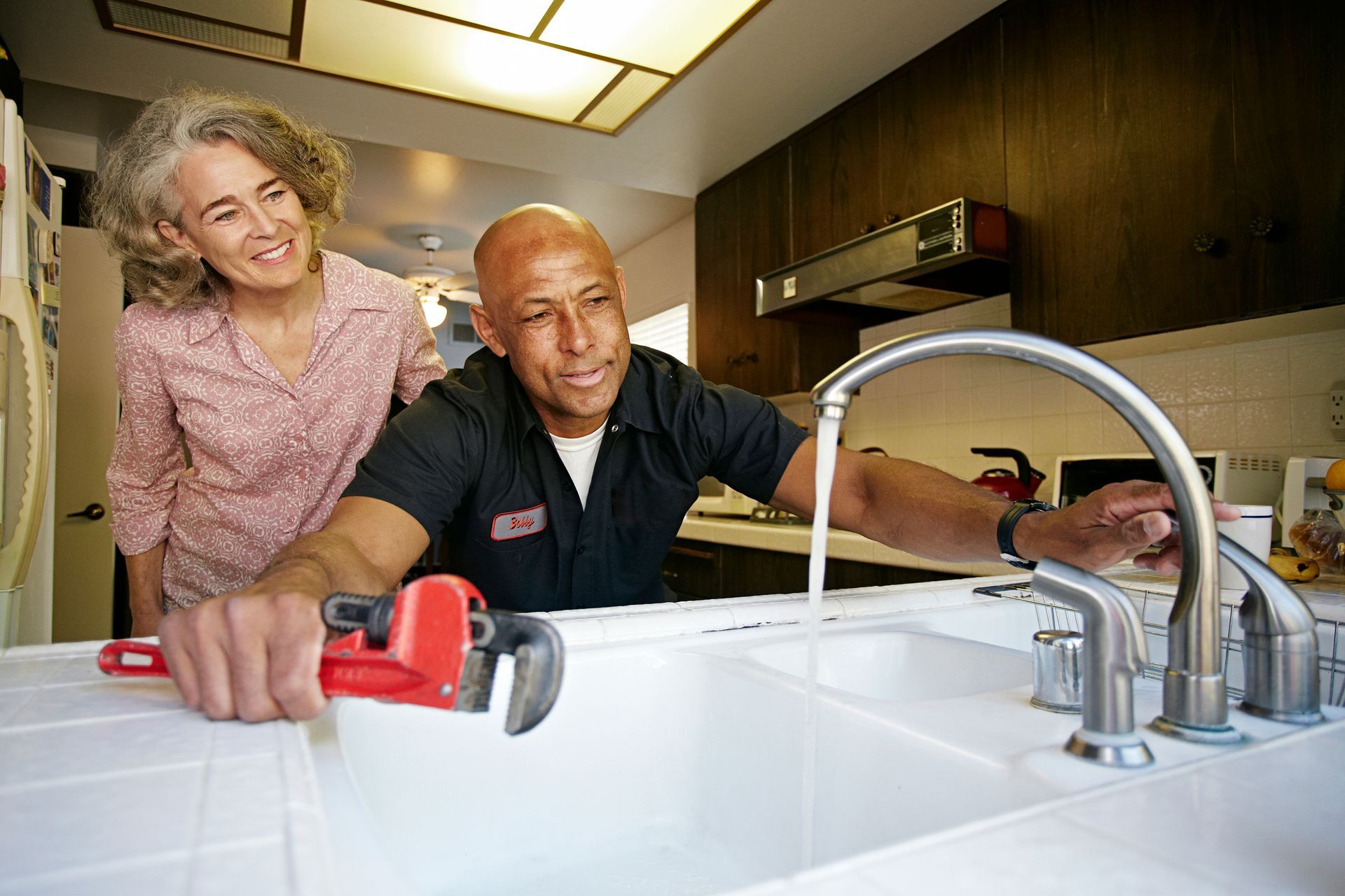 A local plumbing contractor tests the sink for a senior woman after completing plumbing service.