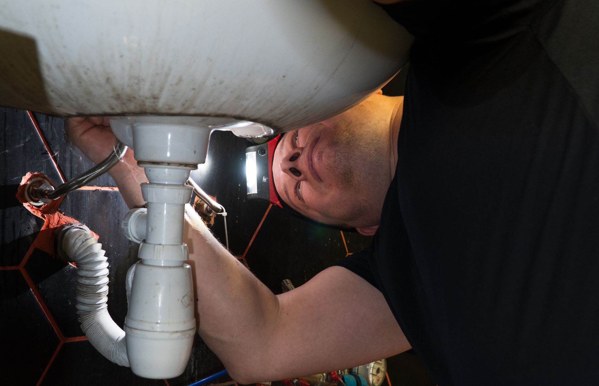 Plumber adjusting drain pipes beneath a sink using tools.