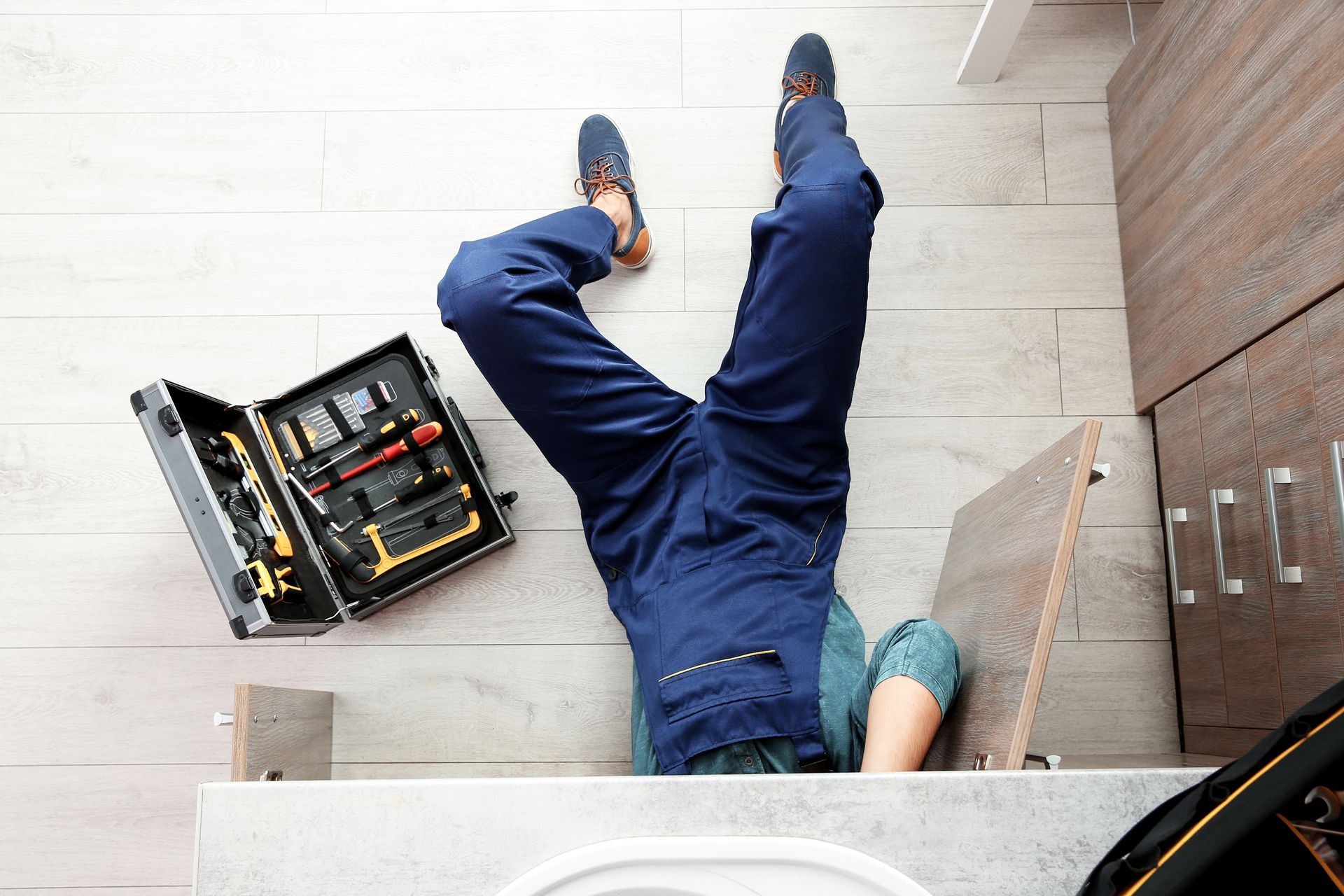 Worker lying on tiled floor while installing flooring, with toolbox open nearby.