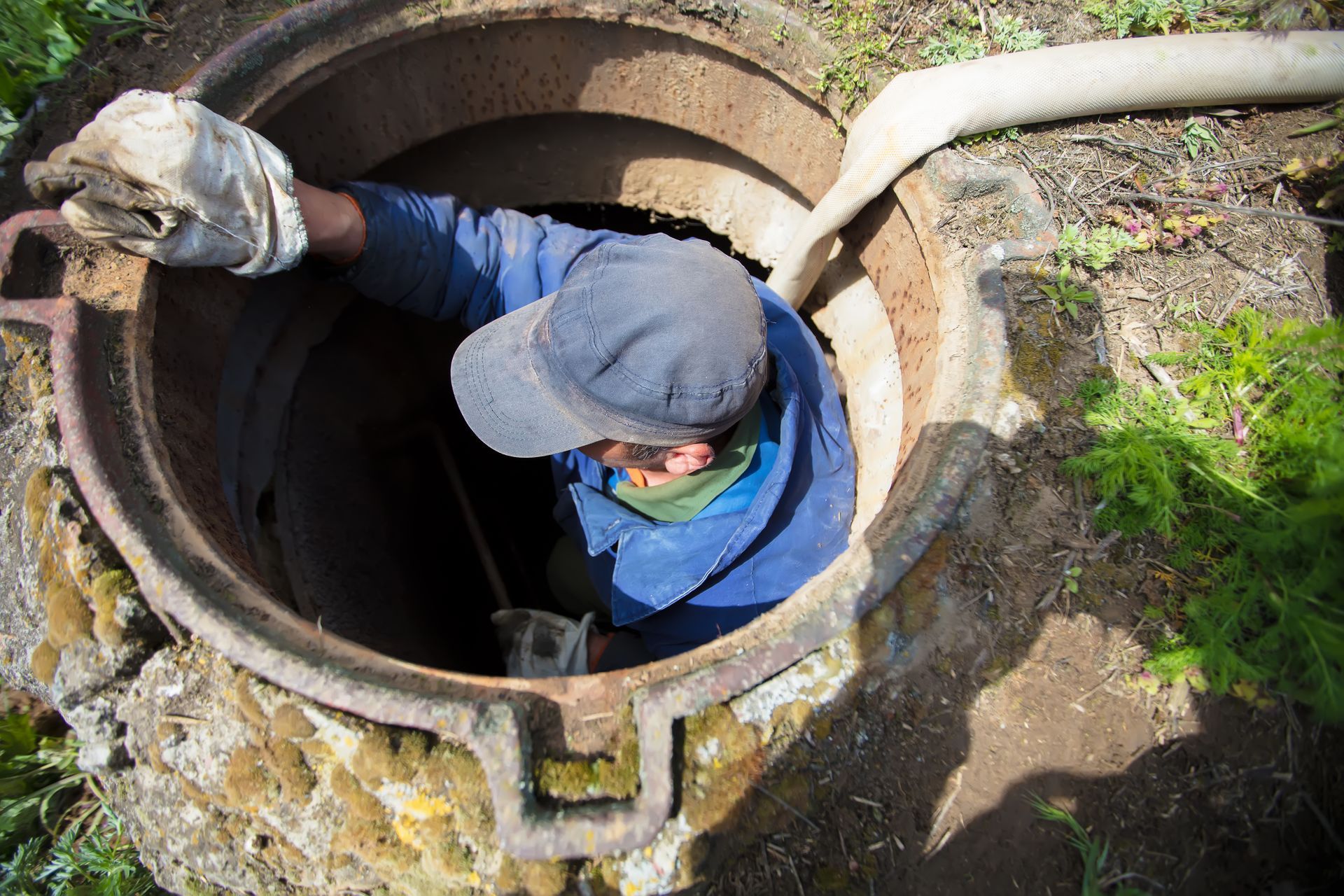 Worker descending into an open manhole while guiding a hose for underground maintenance.
