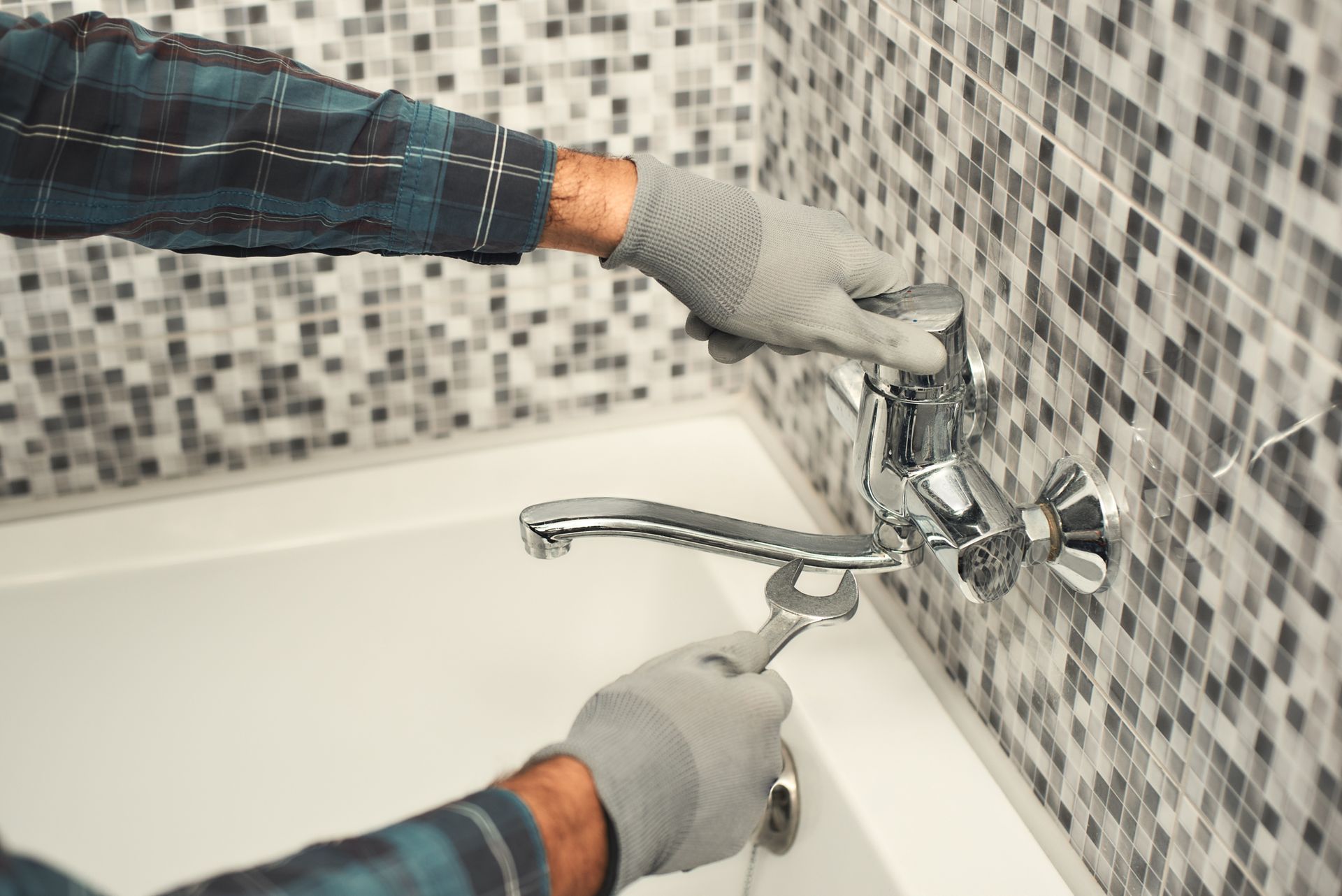 A plumber is repairing a faucet with a wrench in a bathroom.