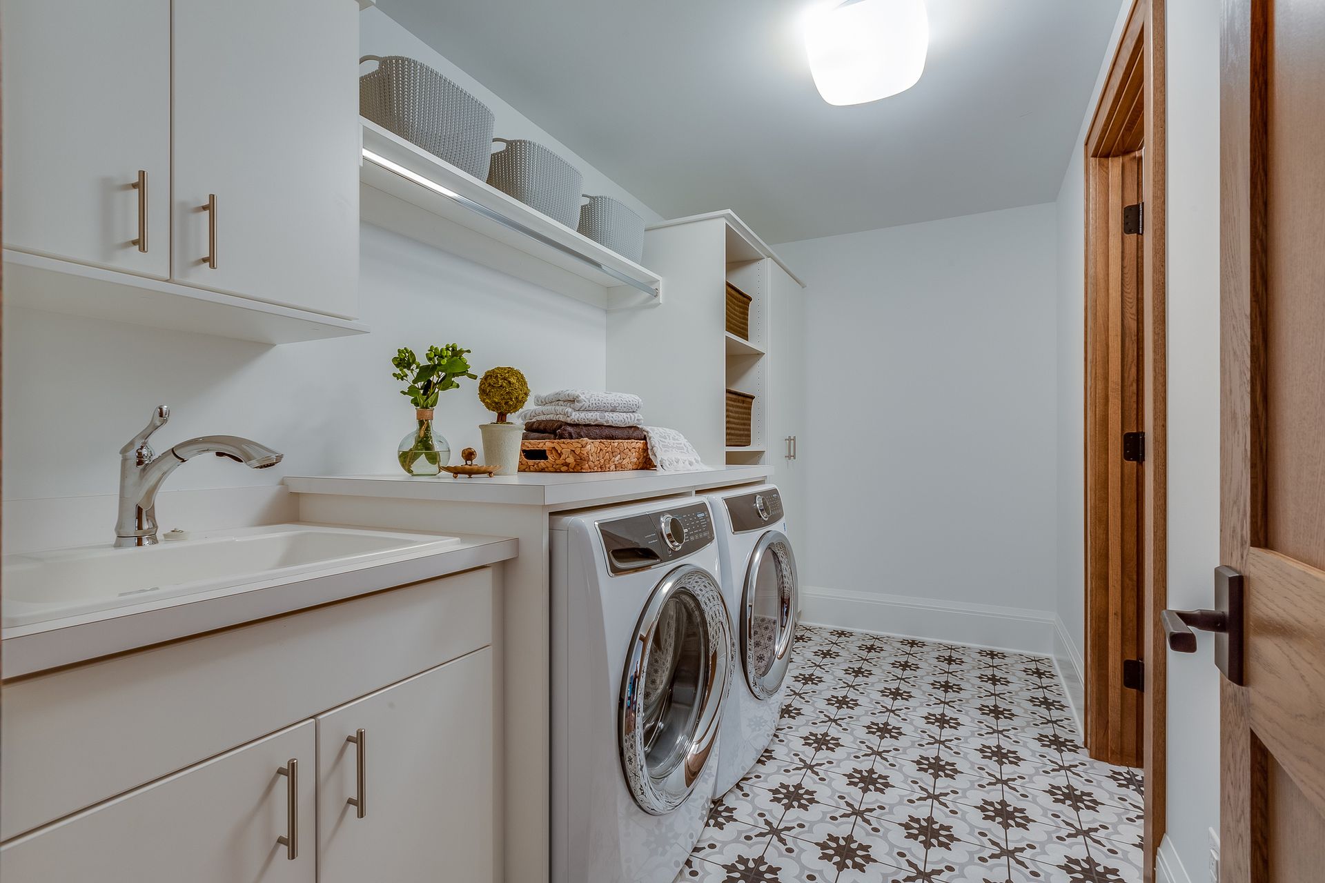 Laundry room with white cabinets, a sink, a washer/dryer, a patterned tile floor, and a wooden door.