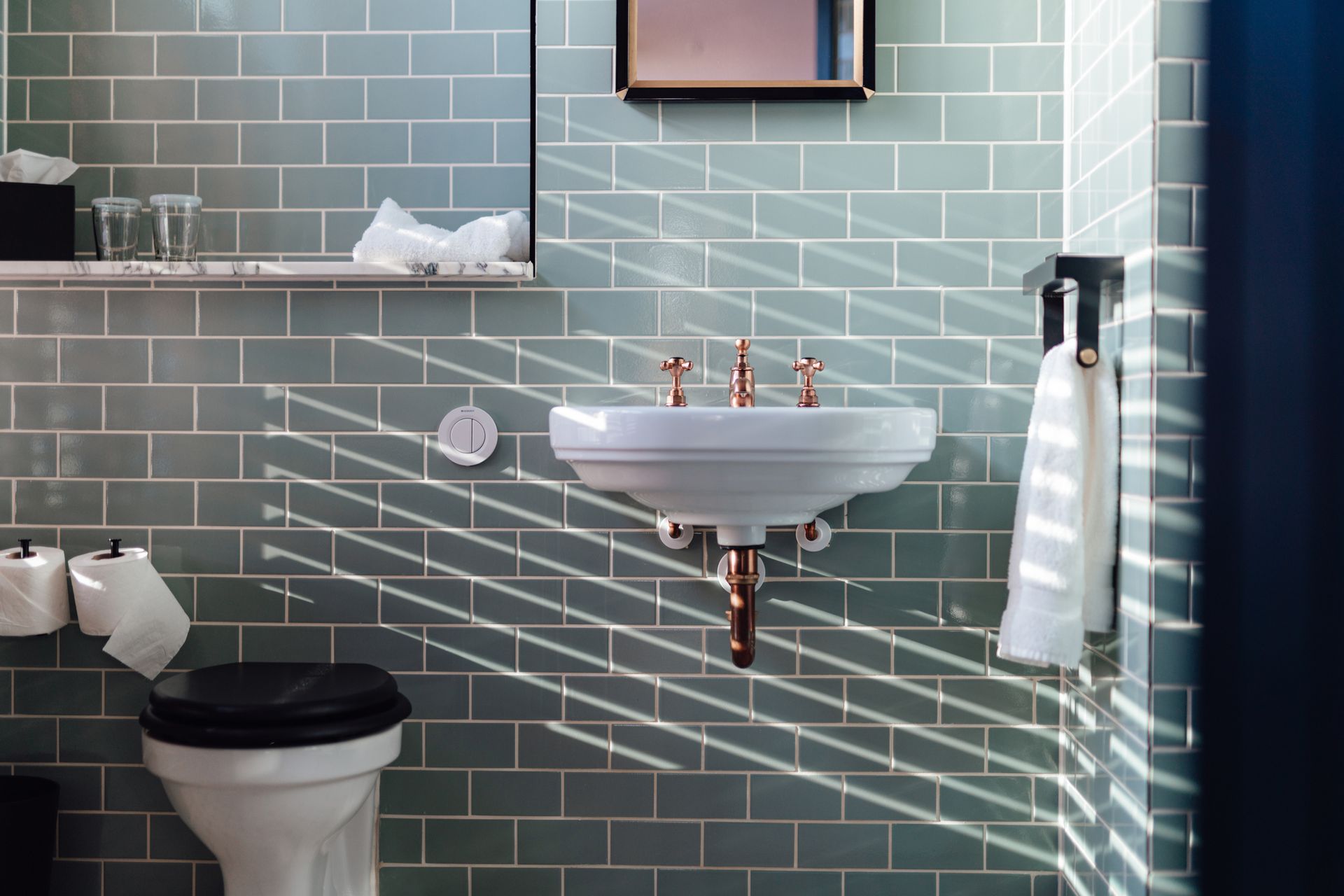 Bathroom with green tiled walls, white sink, and sunlight stripes.