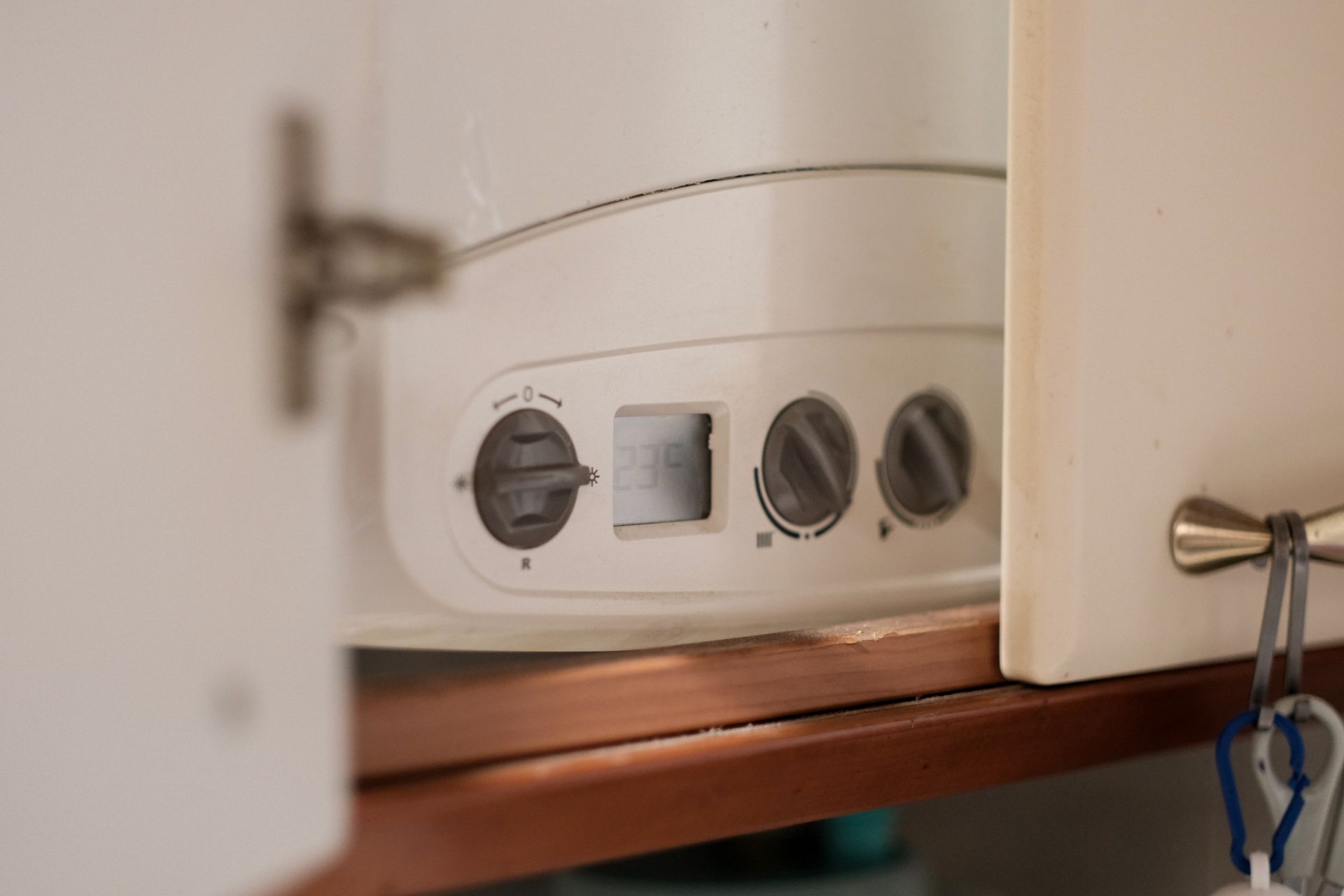 White boiler with three knobs, and open cabinet doors in a kitchen.