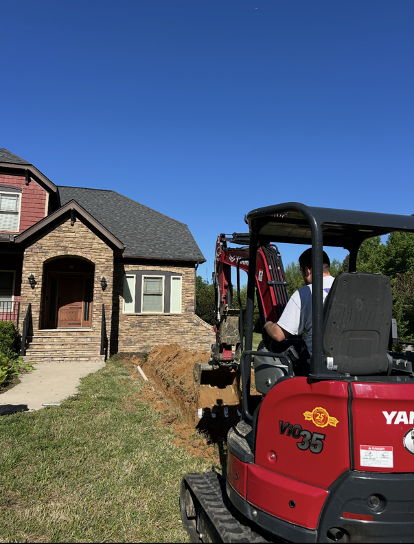 Pipes with blue connectors in a shallow trench, likely for irrigation, surrounded by soil and grass.