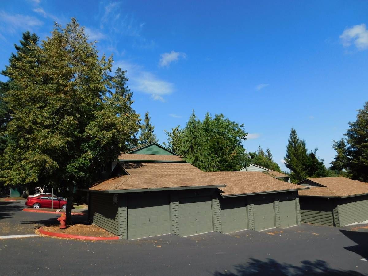 Green buildings with brown roofs; a red car is parked nearby under a blue sky.