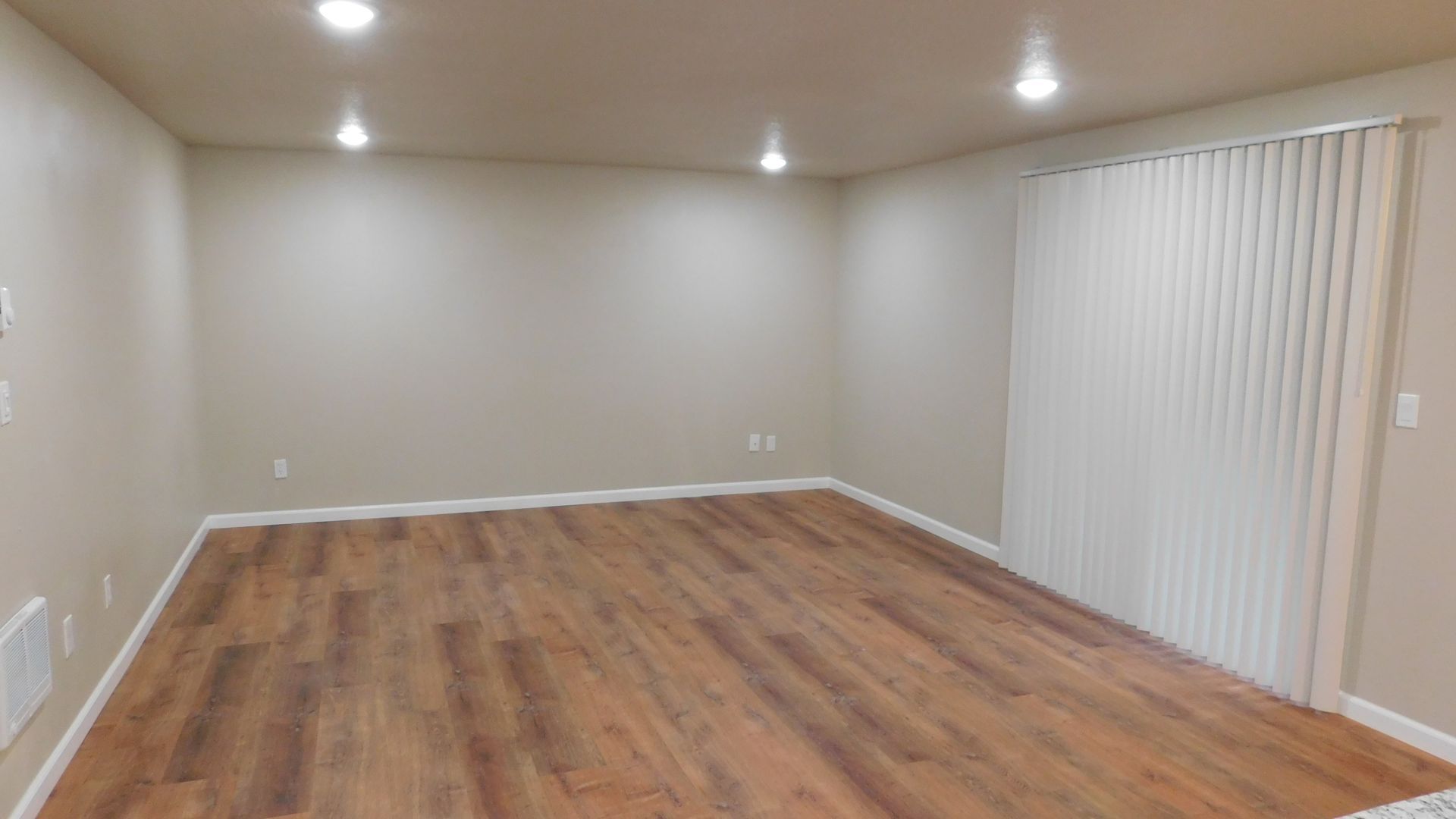 Empty room with wood-look flooring, beige walls, and vertical blinds.