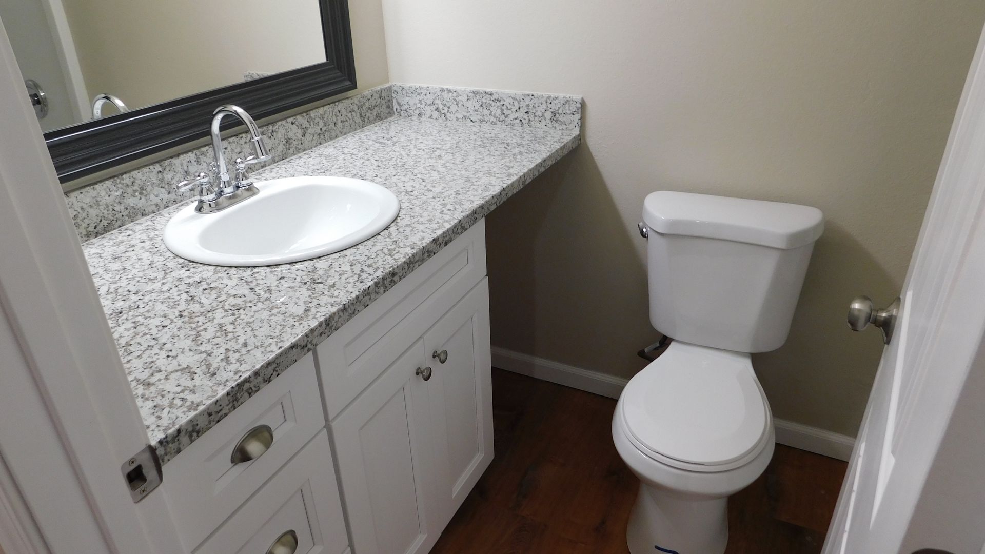 Bathroom with white vanity, granite countertop, toilet, and dark-framed mirror.