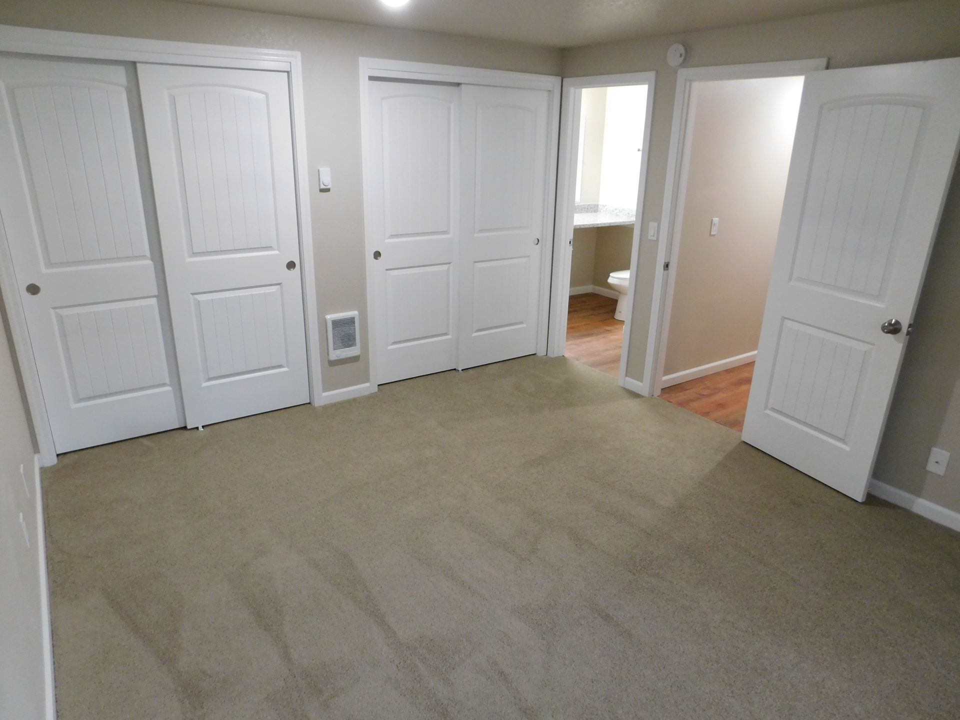 Bedroom with tan carpet, white closet doors, and an open doorway to a bathroom.