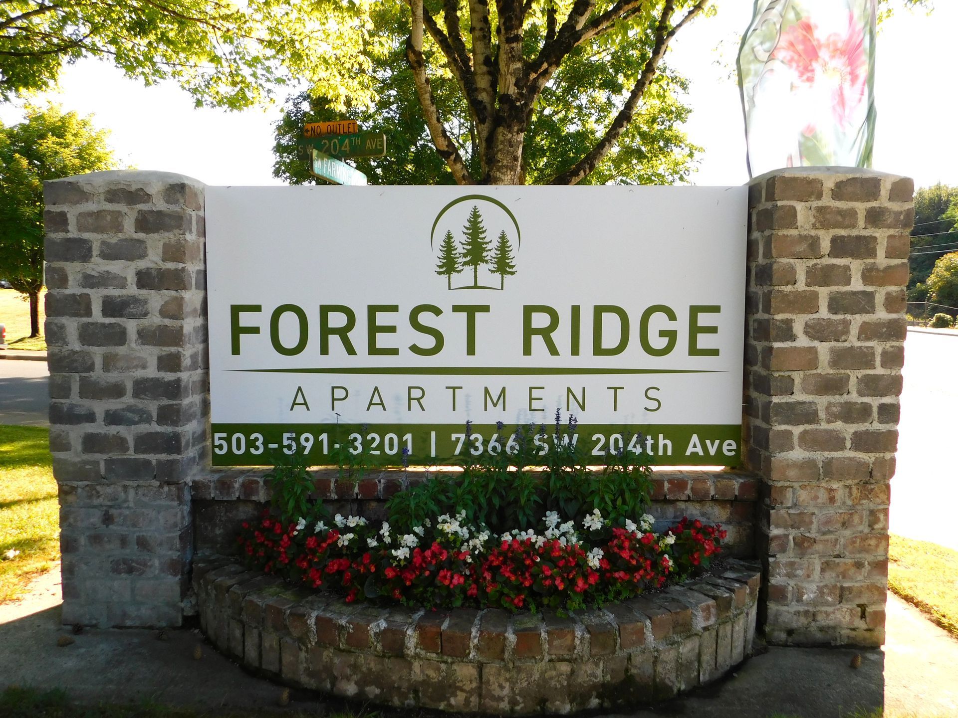 Sign for Forest Ridge Apartments with brick pillars, flowers, and address.