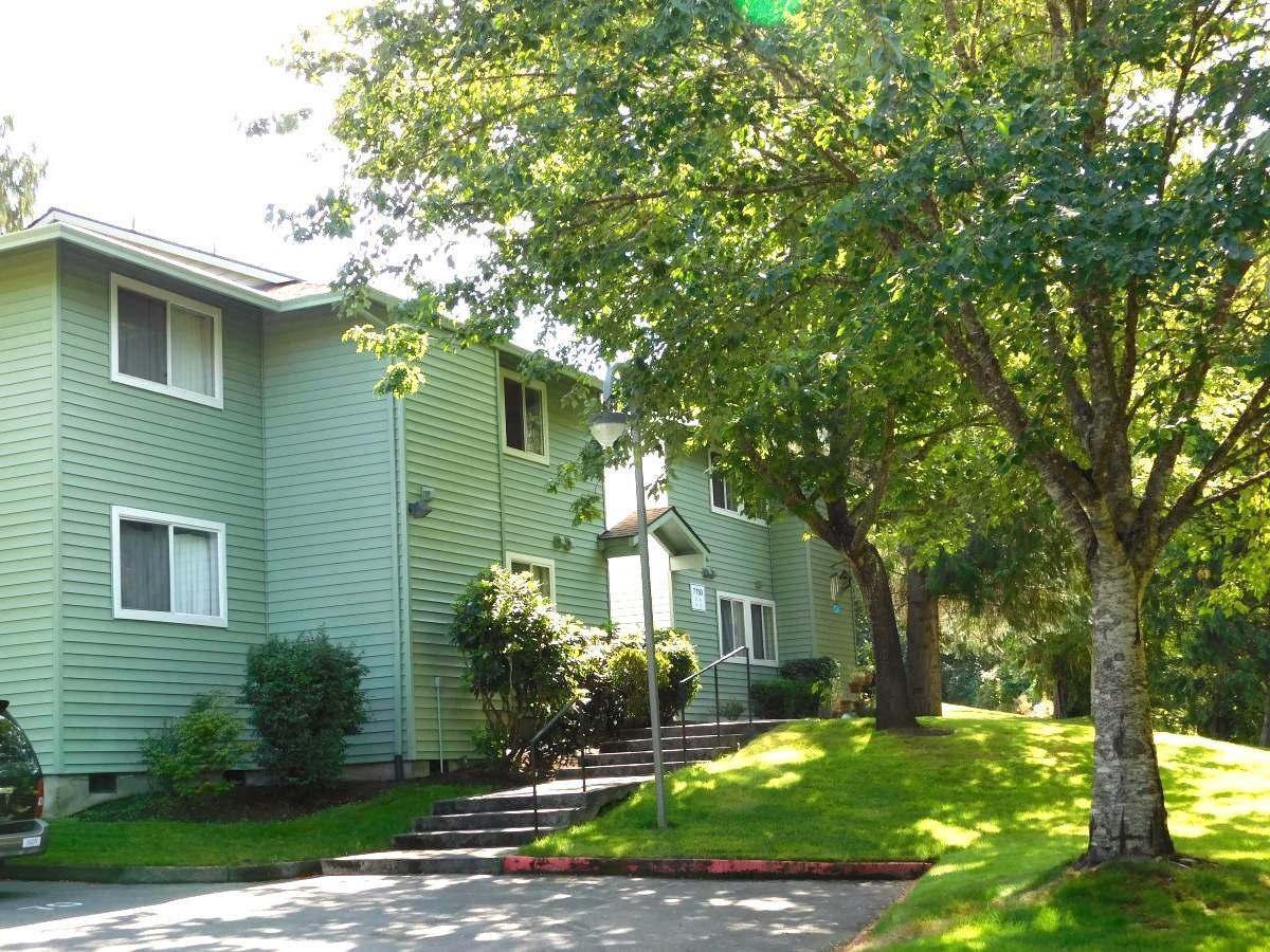 Green two-story apartment building with white window frames and a grassy lawn in front.