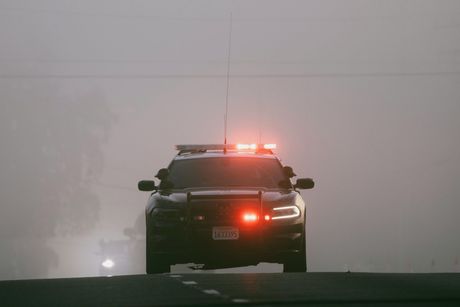 A police car is driving down the road in the fog.