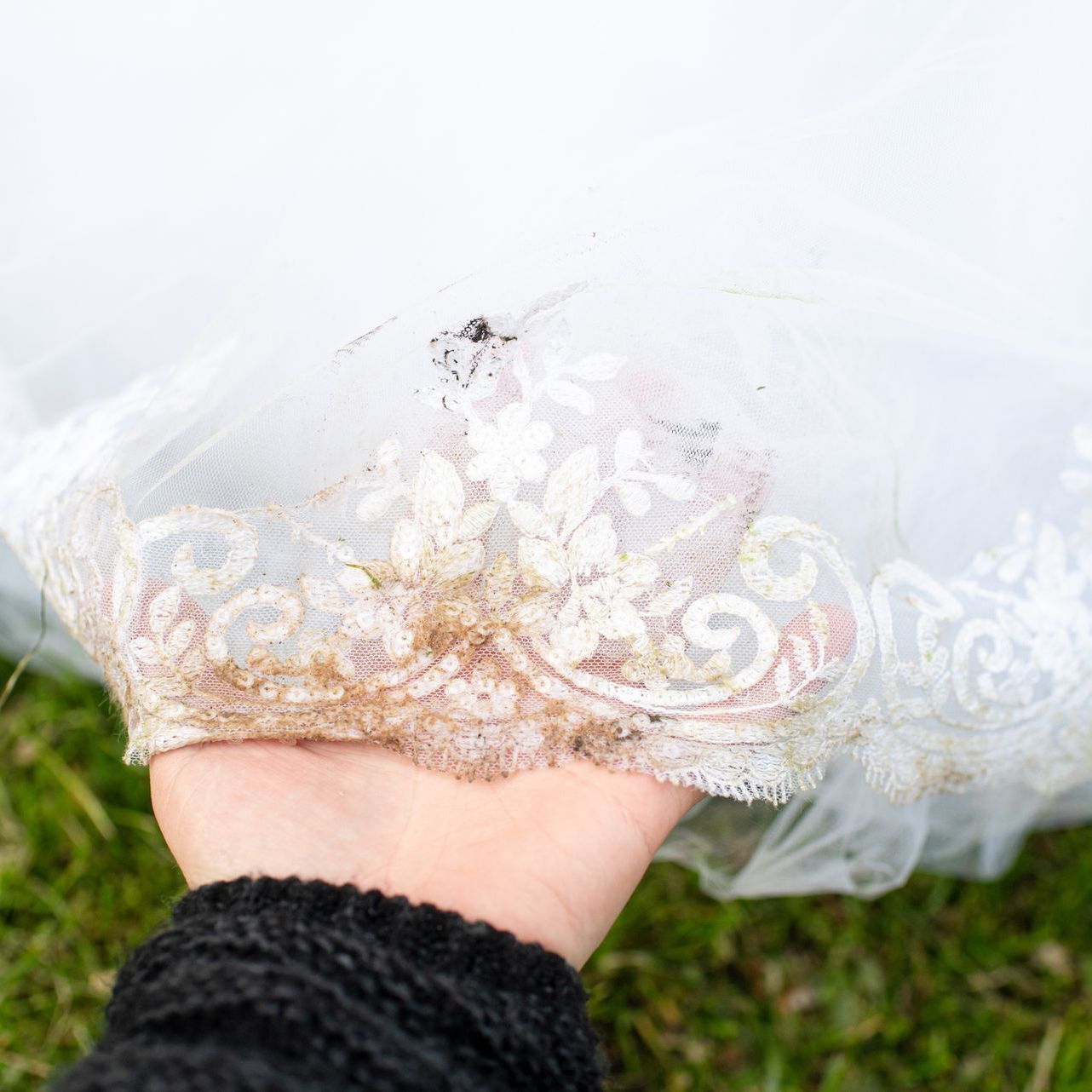 Una persona tiene in mano un abito da sposa sporco.