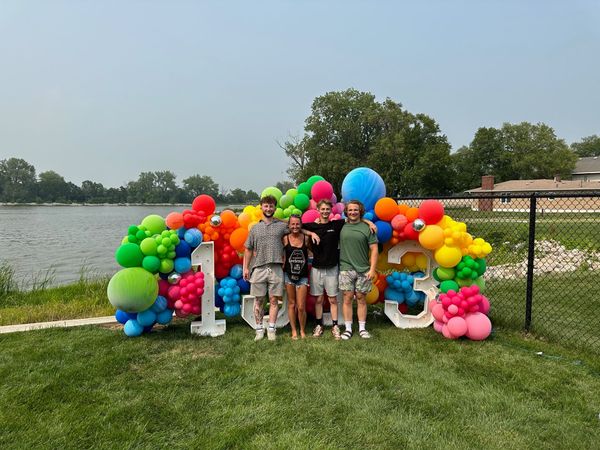 A group of people standing in front of a wall of balloons and marquee lighted letters.