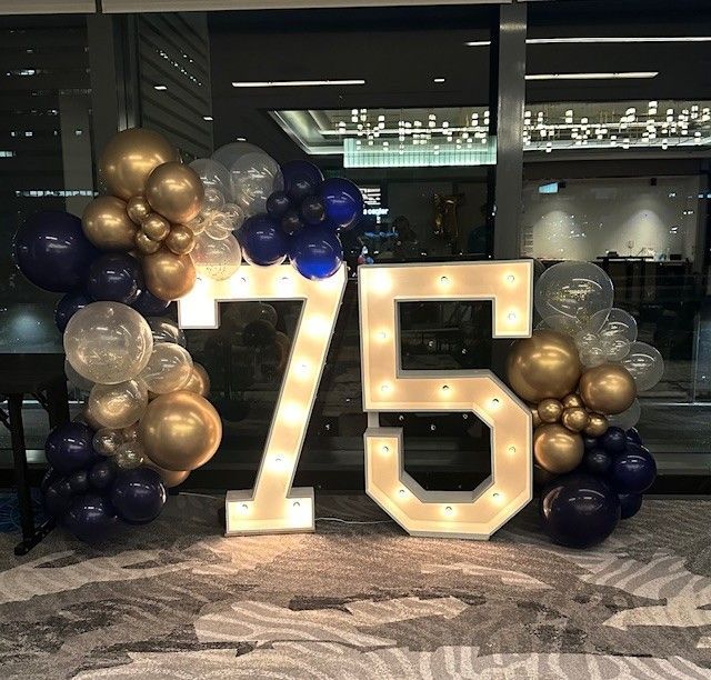 The number 75 is surrounded by balloons and lights