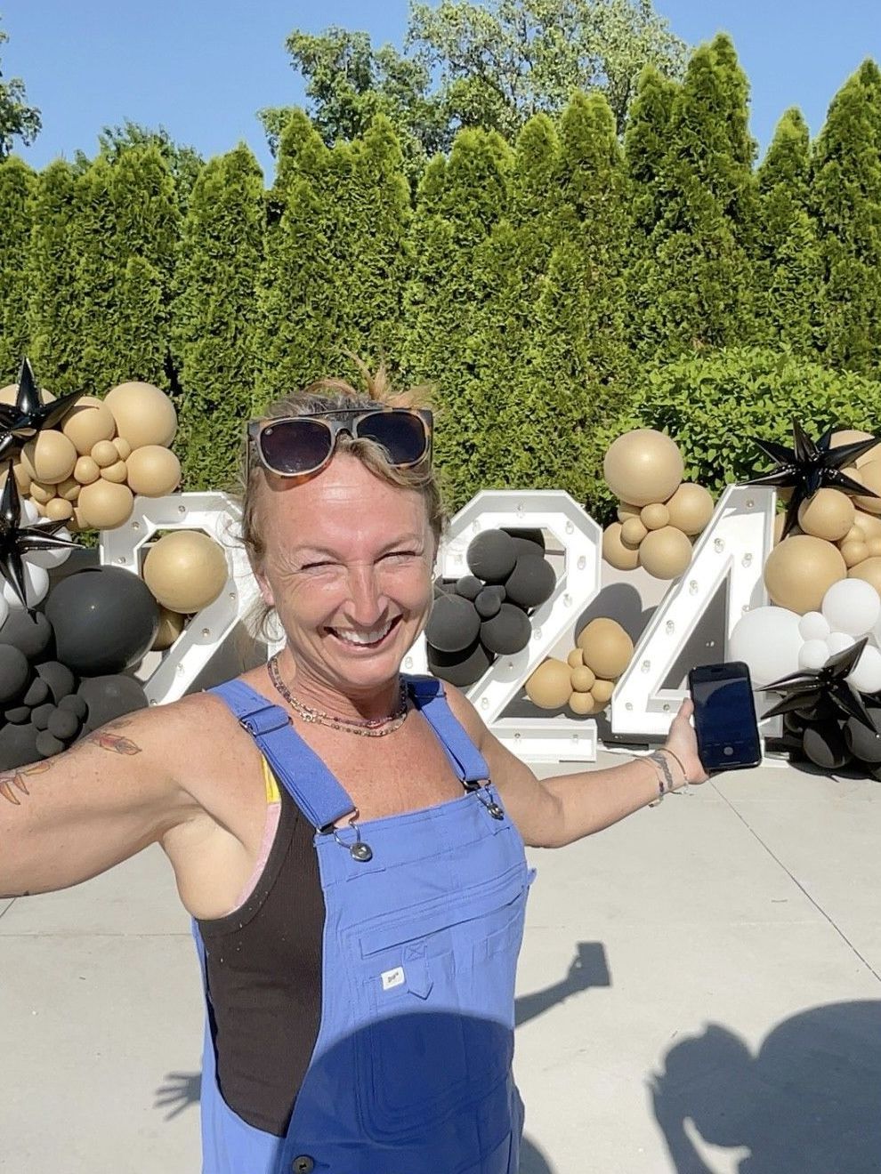 A woman in overalls is standing in front of a sign that says 2024.