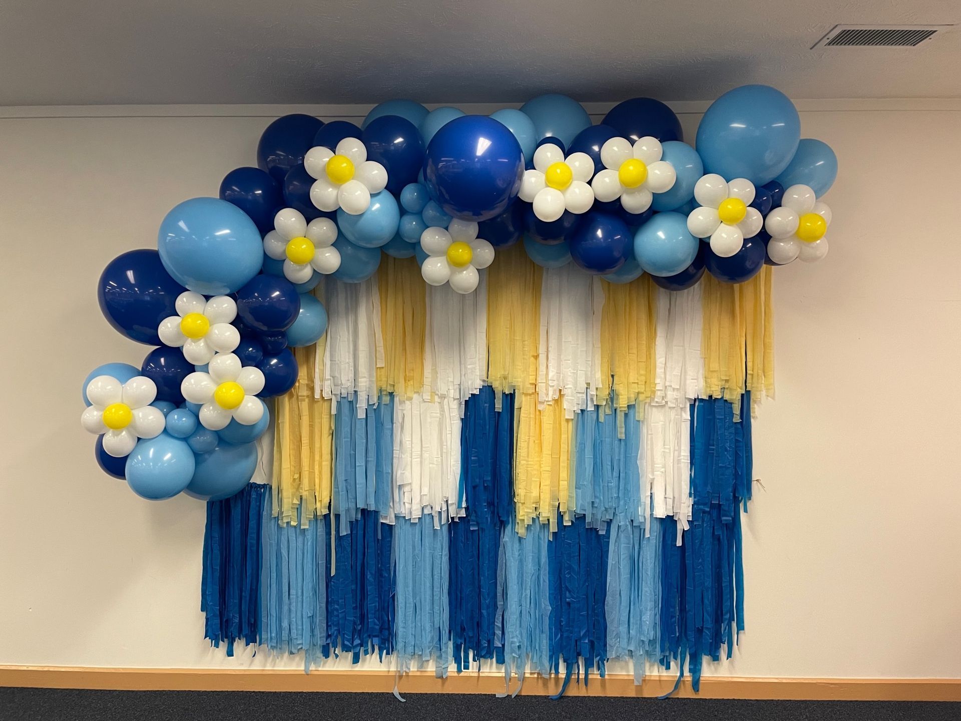 A wall decorated with blue and yellow balloons and flowers