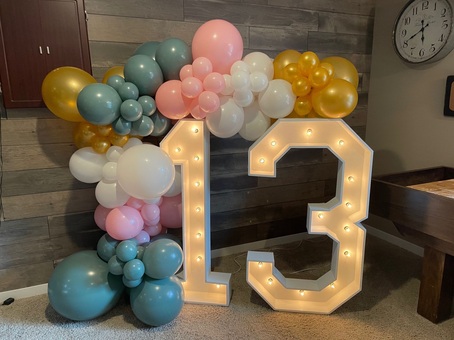 The number 13 is surrounded by balloons and lights in a room.