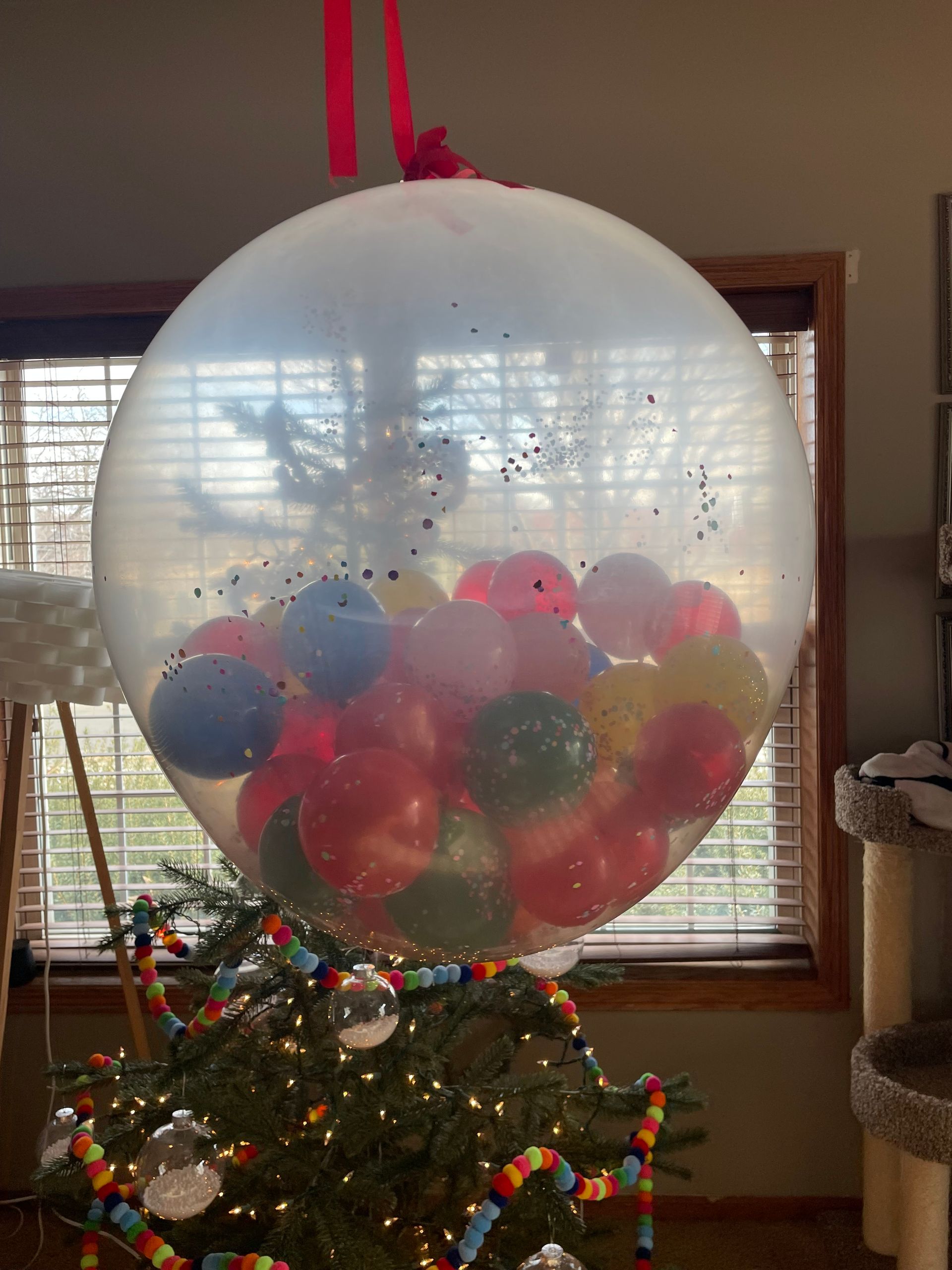 A large balloon filled with balloons is sitting on top of a christmas tree.