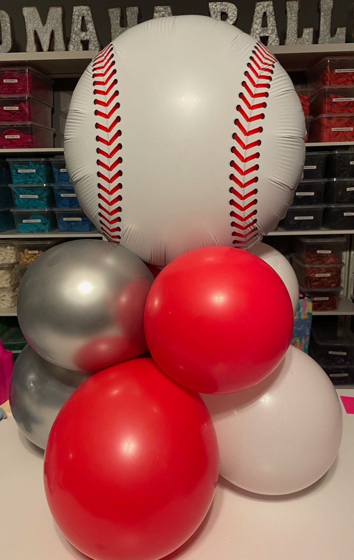 A baseball balloon is surrounded by red and silver balloons.