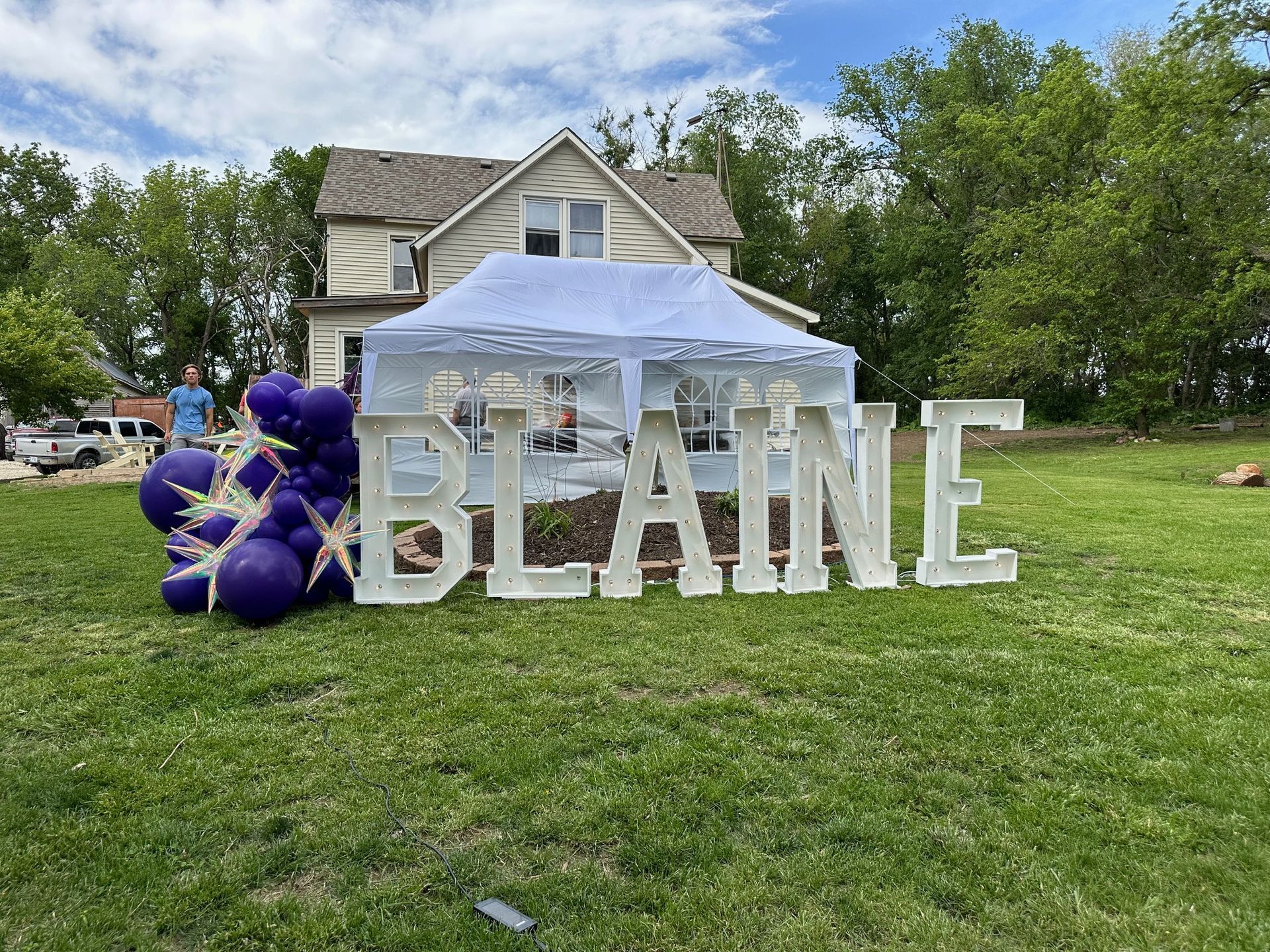 A large white sign that says blaine is sitting in the grass in front of a house.