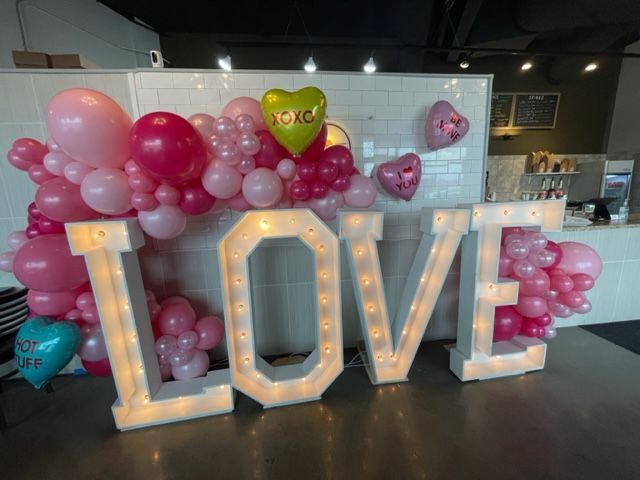 The word love is surrounded by pink balloons and lights.