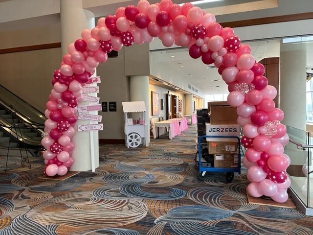 A large pink balloon arch is in a hallway.
