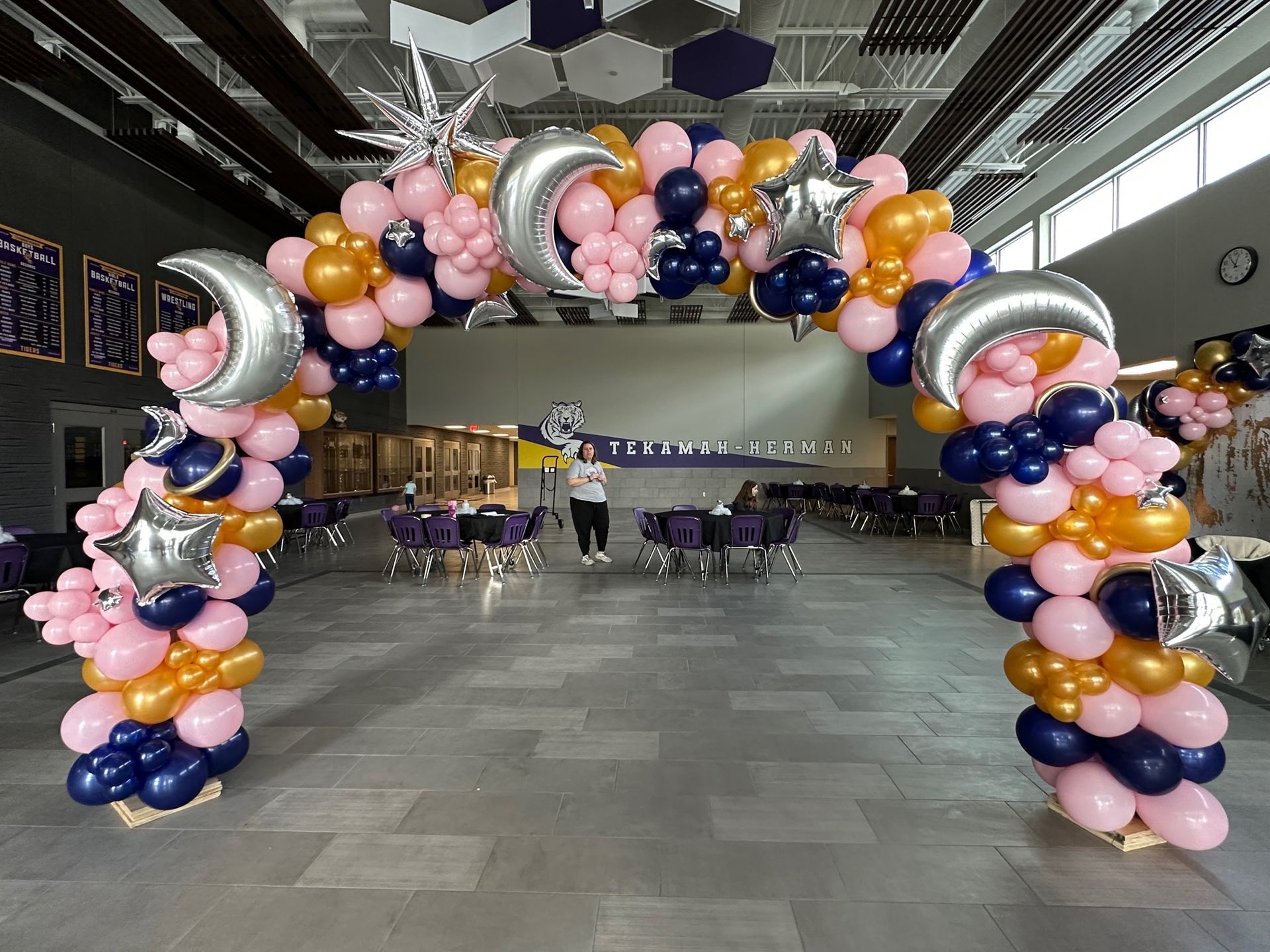 A large arch made of pink , gold , and blue balloons in a room.