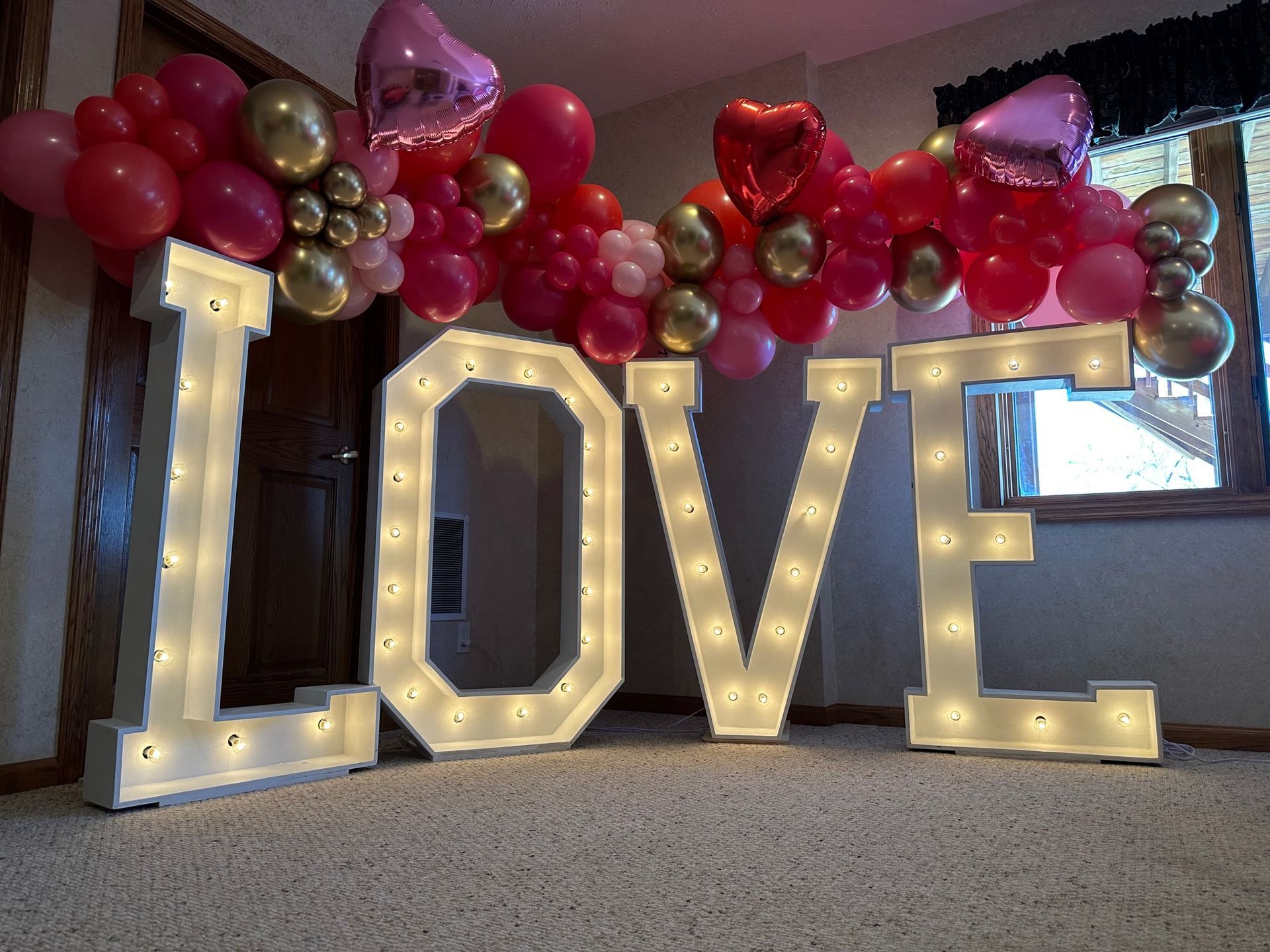The word love is surrounded by balloons and lights in a room.