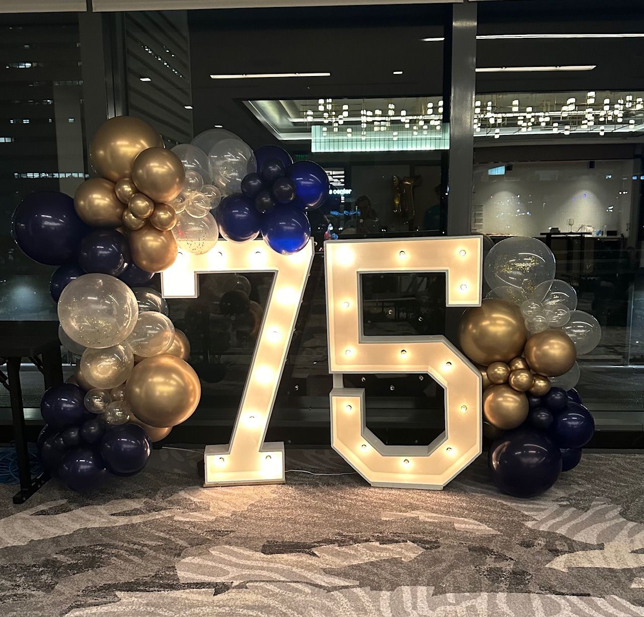 The number 75 is surrounded by balloons and lights