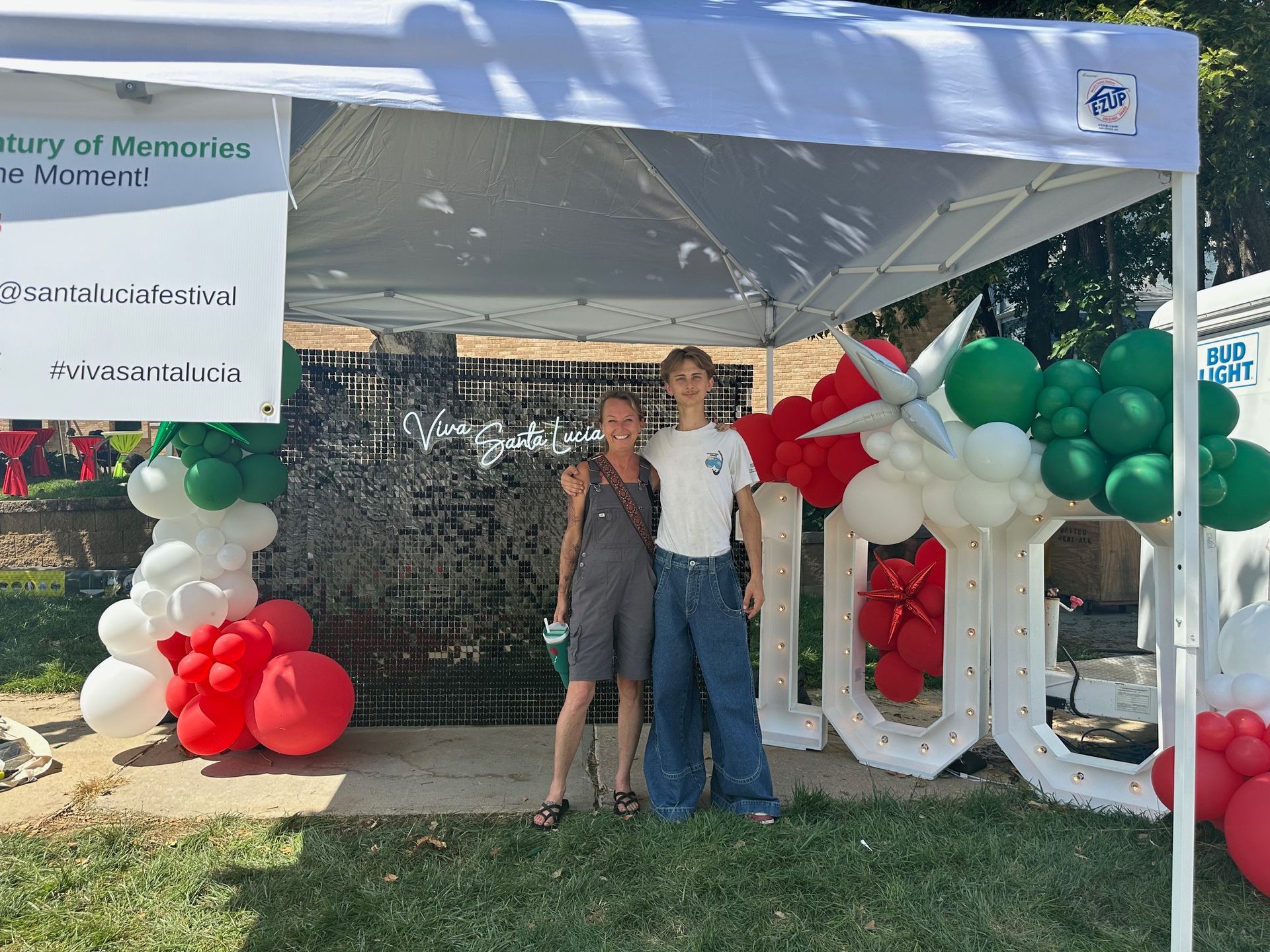 Two women are posing for a picture under a tent with balloons