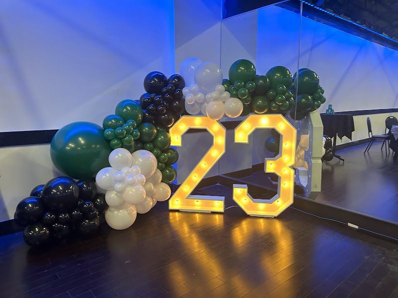 The number 23 is surrounded by balloons and lights in a room.