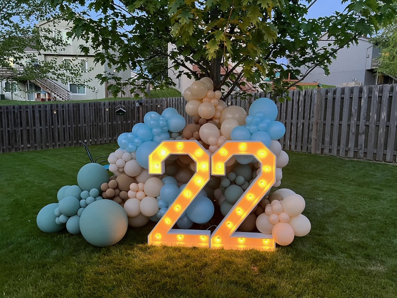A large number 22 is surrounded by balloons in a yard.