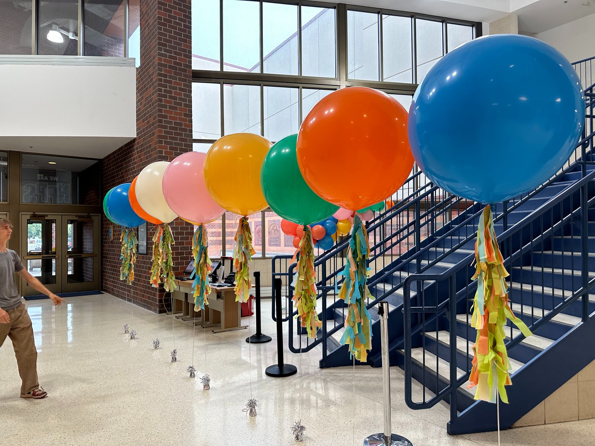 A boy is standing in front of a staircase surrounded by balloons.
