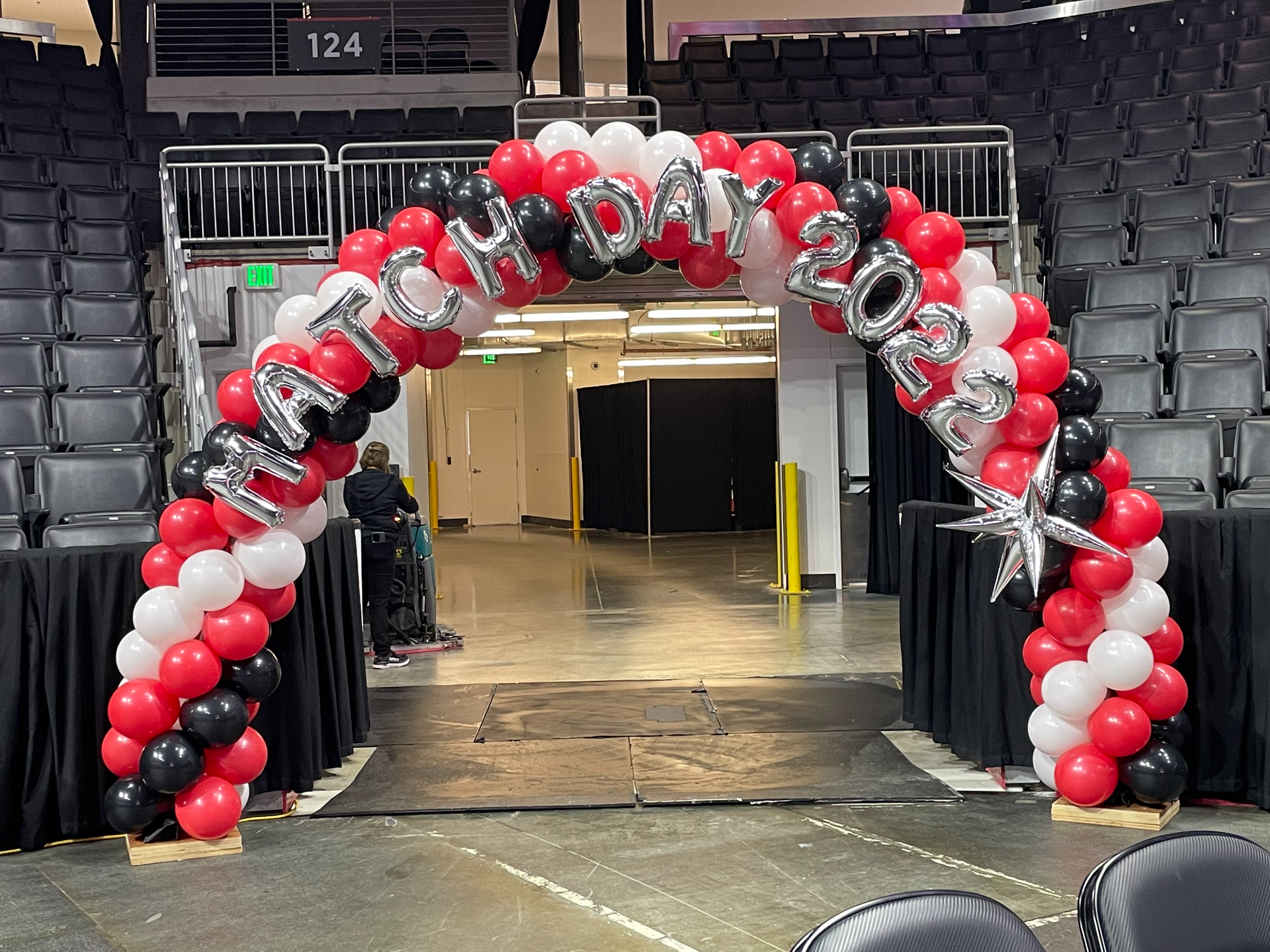 A red , white and black balloon arch in a stadium.